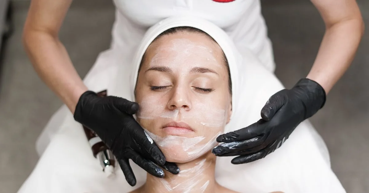 Femme recevant un soin du visage dans un spa, avec une esthéticienne appliquant un masque dans un cadre relaxant.