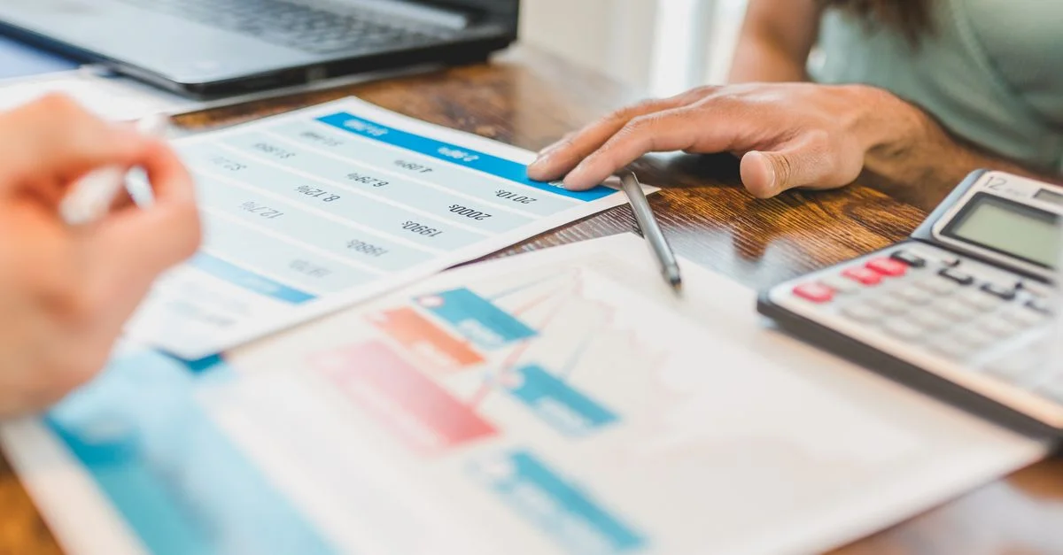 Mains sur un bureau avec des graphiques financiers, une calculatrice et un stylo, analysant des données commerciales.