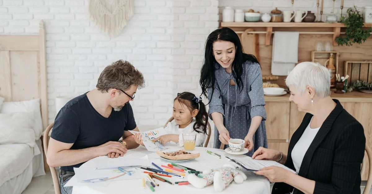 Une famille joyeuse avec une fille adoptée assise et interagissant à une table dans un cadre domestique chaleureux.
