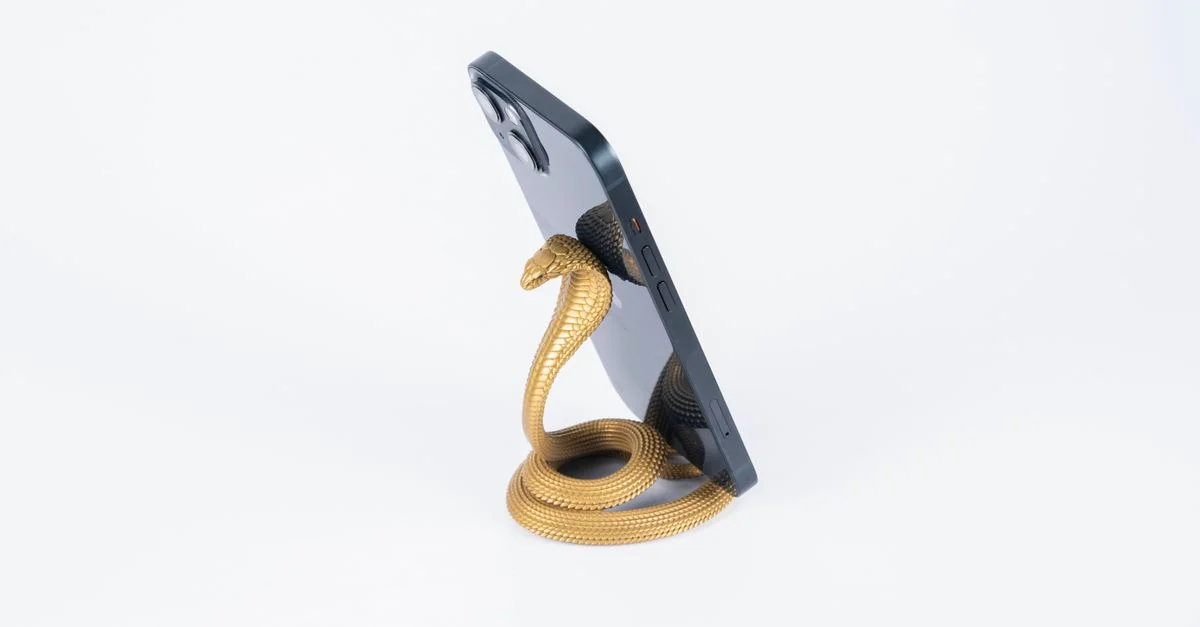 Support de téléphone en forme de cobra doré élégant tenant un smartphone sur un fond blanc.