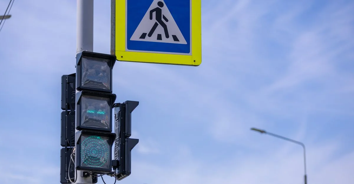Feux de circulation avec panneau piéton à une intersection sous un ciel bleu clair.