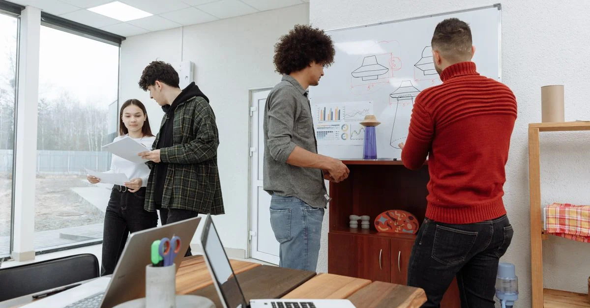 Jeunes professionnels brainstorming dans un bureau moderne avec des ordinateurs portables et un tableau blanc, montrant le travail d'équipe et l'innovation.