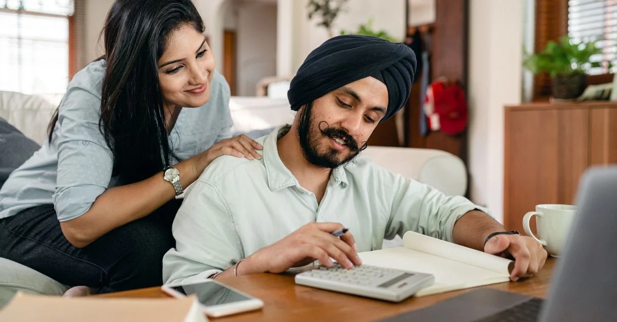Un couple sud-asiatique joyeux examinant leurs finances avec une calculatrice et un carnet à la maison.