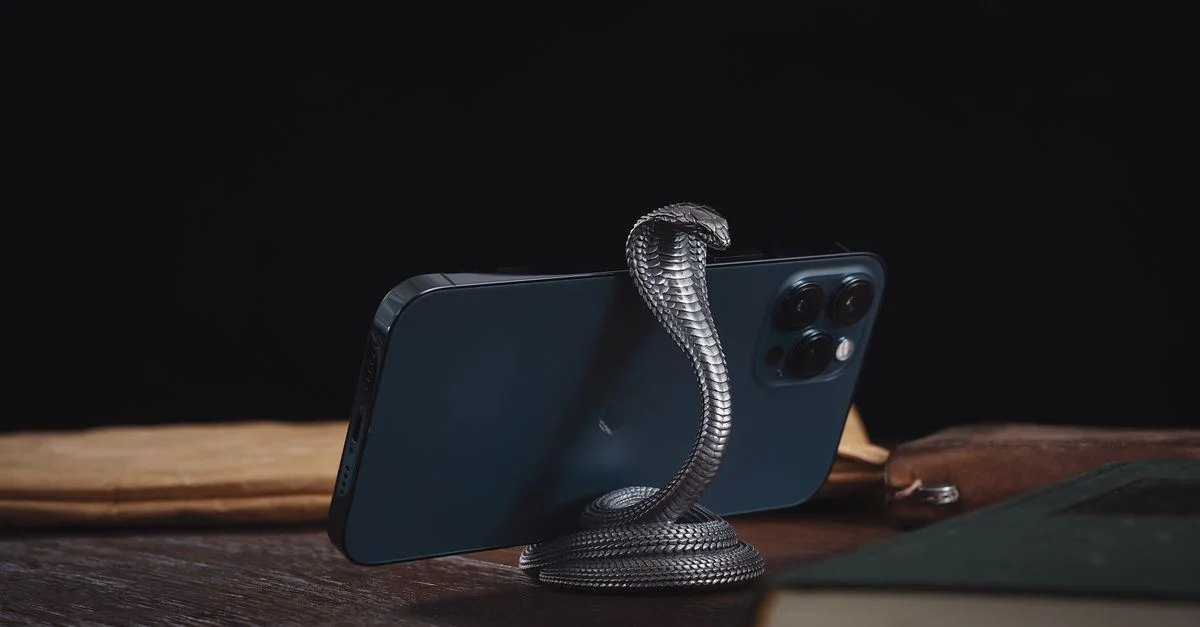 Support de téléphone stylé en forme de serpent tenant un smartphone moderne sur une surface en bois foncé.